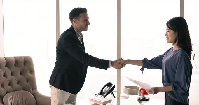 Asian woman applicant enters HR manager office shaking hands, start job interview meeting. Male recruiter welcoming female vacancy candidature, handshaking express respect. Company staffing and hiring