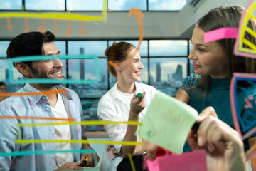 Skilled project manager pointing at glass wall while coworker thinking about plan. Diverse business team working together, brainstorming marketing idea or business plan. Creative start up. Tracery.