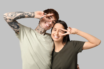 Young couple showing victory gesture on grey background