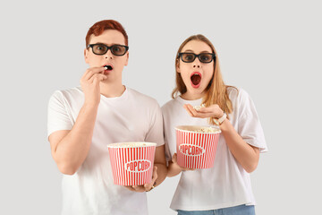 Shocked young couple in 3D glasses with popcorn on white background