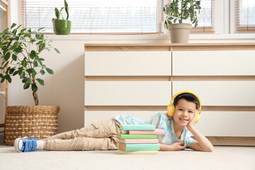 Cute little Asian boy in headphones listening to audiobook with books while lying on carpet in living room