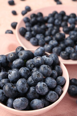 Bowl and plate with sweet fresh blueberries on pink background, closeup