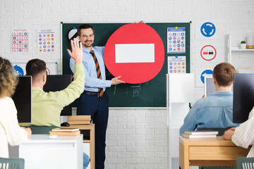 Male instructor with road sign giving lesson to people at driving school