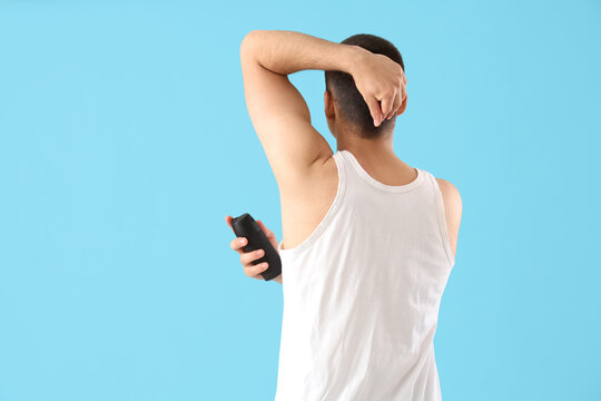 Handsome young man applying deodorant on blue background, back view