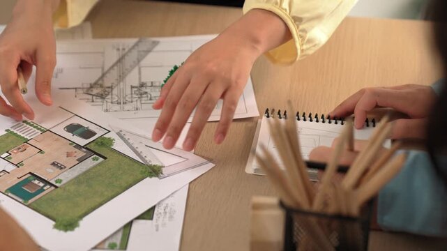 Architects using measurement tool and pencil tracing in building blueprint by coworker support on table with architectural document and wooden block scatter around at office. Closeup. Delineation.