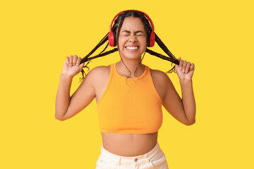Emotional African-American woman listening to music on yellow background