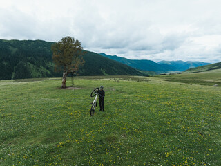 Aerial view of woman riding mountain bike on flowering grassland mountain trail
