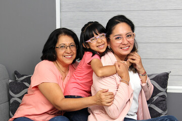Fototapeta premium Three generations of brunette Latina women: grandmother, mom and daughter with glasses show their love and celebrate Mother's Day