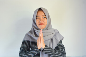 Portrait of smiling beautiful young Asian Muslim woman wearing hijab standing with Eid greeting gesture and welcoming Ramadan isolated on white studio background