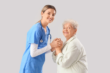 Senior woman with nurse holding hands on light background