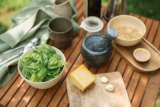 Close-up of basil, parmesan, garlic, pine nuts and olive oil on a table for making fresh basil pesto sauce in a summer garden