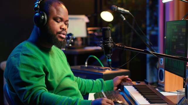 Professional artist writes new verses for a song in home studio, producing new music with mixing console and pc software. Composer works with audio equipment and tools, recording tunes. Camera A.