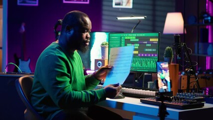 Artist pointing at musical sheet notation to explain notes on piano, teaching people to play synthesizer in home studio. Composer musician playing midi controller during online master class. Camera A.