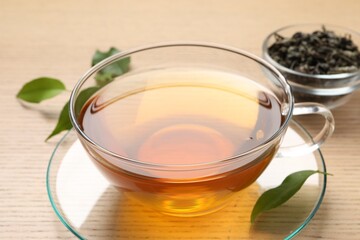Refreshing green tea in cup and leaves on wooden table, closeup