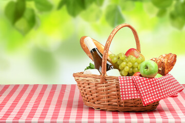 Picnic basket with foods and wine on table in nature. Space for text