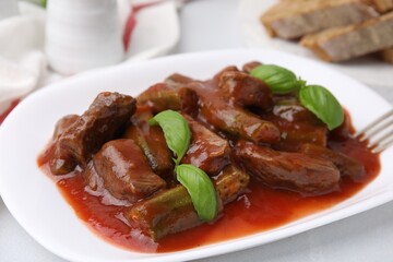 Tasty stew with okra, tomato sauce and basil on white tiled table, closeup