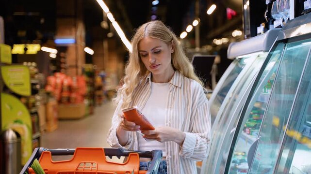 Beautiful housewife chooses salmon in the freezer section of a supermarket, exploring options