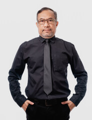 Asian man in a black shirt and tie stands with his hands in his pockets. He has a serious expression on his face