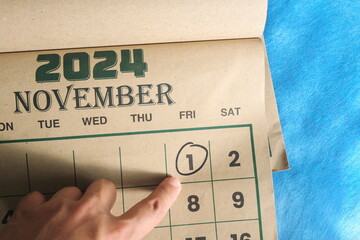 Hand pointing on November 1 2024 date on calendar flat lay in blue background. First day of the month reminder.