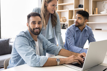 Portrait of handsome business team leader man typing at laptop, meeting with group of colleagues at computer for teamwork, showing online content to speaking diverse coworkers, looking at camera