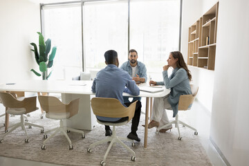 Small business team of three sitting at large meeting table for work discussion, brainstorming on...