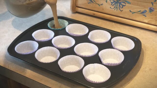A man pouring cupcake batter into a backing pan.