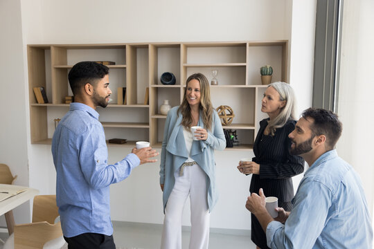 Multiethnic office friends enjoying work break in co-working space, drinking hot coffee together, discussing job, career, projects over cup of tea, enjoying offline communication