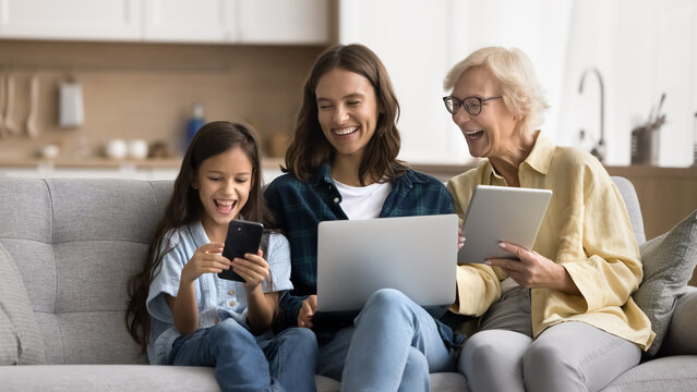 Happy kid, young mother and blonde mature grandmother using gadgets and having fun at home, holding tablet, laptop and smartphone, enjoying Internet technology, communication. Banner shot - Powered by Adobe