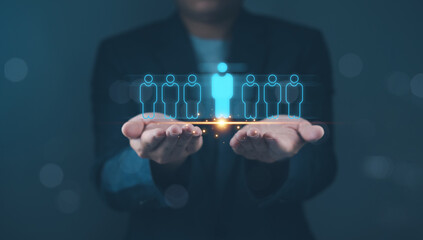 Hands holding holographic figures with one highlighted. Studio shot with blurred person in background. Recruitment and human resources concept for banner and poster