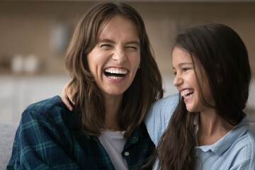 Cheerful excited mother and sweet daughter child laughing out loud emotionally, sitting close,...