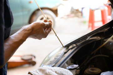 A close-up of a person checking the oil level in a car engine using a dipstick. The hand holds the dipstick carefully, inspecting the oil mark against a blurred background of the engine bay.