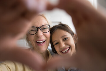 Positive excited granny and happy grandkid girl showing hand heart, gesture of friendship, love,...