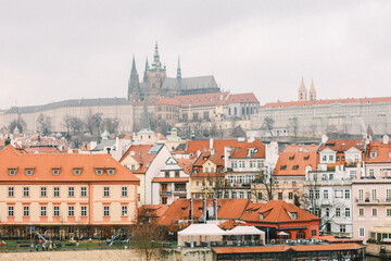Obraz premium Foggy cityscape in the evening, view at winter Prague Castle Pražský hrad panorama, medieval old european town with cathedrals, St. Vitus Cathedral, orange tiled roof 