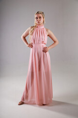 Beautiful young blonde woman in pink dress on grey background full length