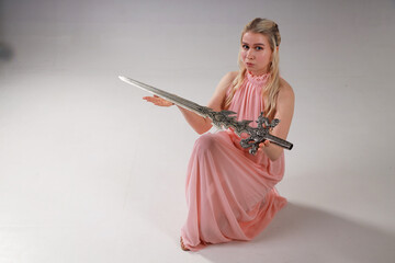 Beautiful blonde woman in pink dress holding a sword