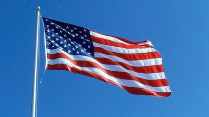 Obraz premium A close-up of an American flag waving in the wind against a clear blue sky, the stars and stripes clearly visible, symbolizing patriotism and freedom, evoking a sense of pride and national identity,