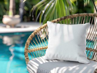 A white pillow sits on a wicker chair by a swimming pool.