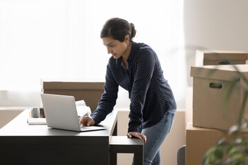 Businesswoman review orders, check dispatch schedule, contact to courier to shipping parcels boxes of bought goods of electronic commerce clients. Small business owner workflow use laptop in warehouse