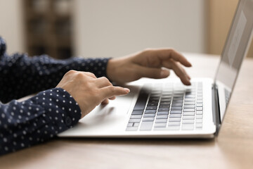 Unknown female sits at table using modern laptop for work, study or fun, prepare report, teleworking from home-office, chatting on-line with friend, share messages or e-mail by business. Wireless tech