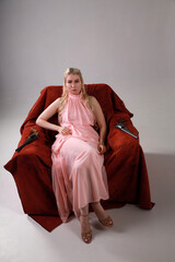 Pretty blonde woman in pink dress with two revolvers sitting in a red armchair