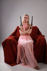 Pretty blonde woman in pink dress with two revolvers sitting in a red armchair