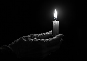 Black and white photography of an old woman's hand holding a candle, dark background with light coming from the flame. The photograph is in the style of a minimalist portrait. 