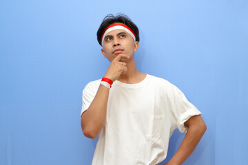 Indonesian man in white shirt and Indonesian flag posing thinking gesture with hold his chin and eyes looking up,Indonesian independence day concept.