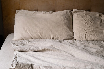 Wrinkled bed with beige pillows and sheets in cozy bedroom.