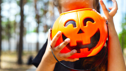 Closeup of unrecognizable little girl wearing Halloween costume and holding pumpkin basket in trick...