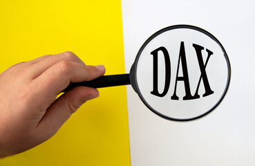 Hand holding magnifying glass over DAX abbreviation on yellow and white background