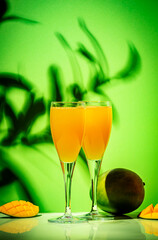 Summer alcoholic cocktail with champagne, mango juice, syrup and ice, green background, hard light
