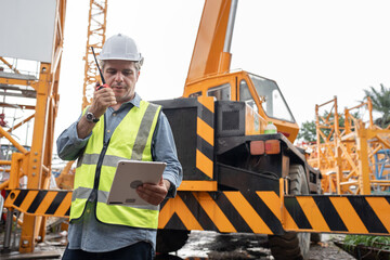 Caucasian mature engineer man worker use tablet computer and walkie talkie working with crane truck...