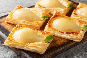 Hasselback pear in puff pastry fresh from the oven closeup on the wooden board on the table. Horizontal