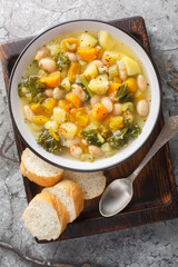 Tuscan Bean and Vegetable Soup Zuppa alla Frantoiana closeup on the bowl on the wooden board. Vertical top view from above